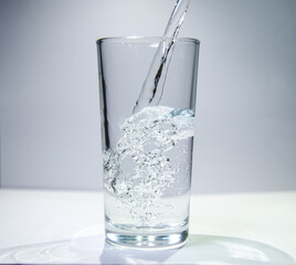 A stream of water flows into a transparent glass The water swirls at the bottom of the glass.