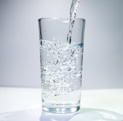 A stream of water flows into a transparent glass The water swirls at the bottom of the glass.