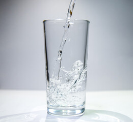 A stream of water flows into a transparent glass The water swirls at the bottom of the glass.