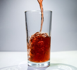 A stream of raspberry drink flows into a transparent glass The drink swirls at the bottom of the glass