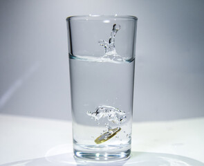 A euro coin falls into a glass of clear water Splashes are visible from above the water