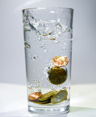 Several coins fall into a glass of clear water Air bubbles are visible in the water