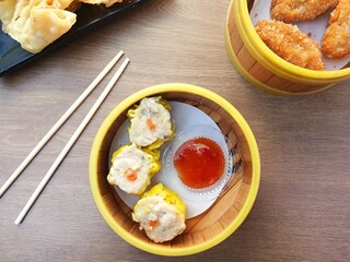 Delicious dim sum and spicy Thai sauce served in bamboo klakat, with bamboo chopsticks on wooden table.