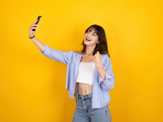 Happy young brunette caucasian woman in 20s standing over isolated yellow studio background doing...