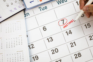 Close-up view of hand using pen to draw red circle on calendar with write word Meeting. Concept of...