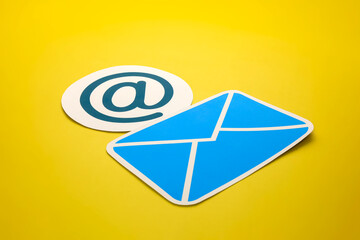 Paper letter and at sign on yellow background, with copy space. Business concepts of online contact channels, and electronic mail inbox notifications.