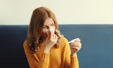 Sick woman sneezing blow nose with tissue, measuring checking body temperature looks at thermometer