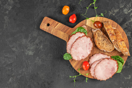 Sliced smoked pork is beautifully arranged with fresh spinach, multigrain bread, and colorful cherry tomatoes on a rustic wooden serving board