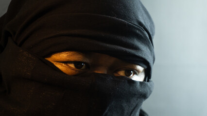 Close-up of masked male face lit by warm ambient light on black background, dramatic and secretive...