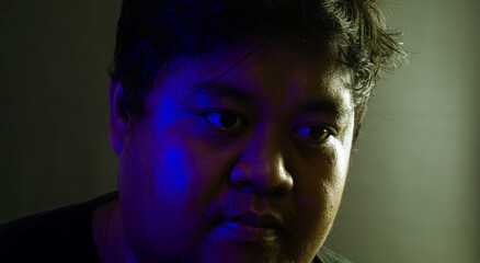 Close-up male face partially lit by blue ambient light against black background, mysterious and...
