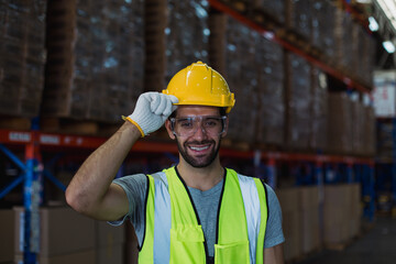 Confident male warehouse worker wearing safety vest and helmet smiling at camera in industrial storage facility.  Professional staff in warehouse concept