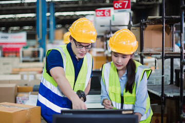 Asian warehouse workers using barcode scanner and computer to manage inventory in modern logistics center. Focused teamwork in industrial environment.