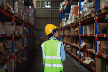 Southeast Asian female warehouse worker wearing safety helmet and reflective vest walking through...