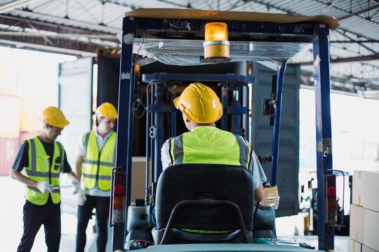 Forklift operator loading cargo into truck at warehouse dock with workers assisting, highlighting teamwork, logistics coordination, and transportation efficiency.