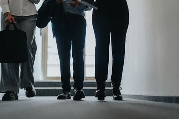 A group of business people walking with purpose in a modern office hallway, reflecting...