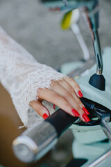 The hand of a girl in a lace dress on the handlebars of a Vespa motorcycle. Red nails. Manicure. The Italian mood