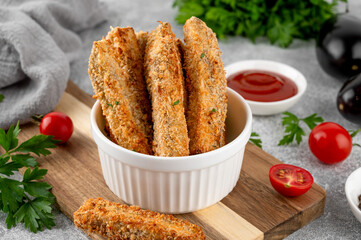 Baked crispy eggplant sticks served with tomatoes sauce in a white ceramic bowl on a gray concrete background. Vegetarian healthy dish. Selective focus