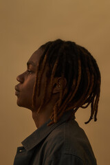 Black young adult man standing in profile view against plain background, showing serious facial...