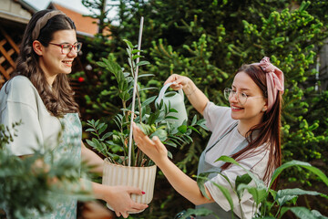 Two female friends or sisters taking care of plants with water can and mister	
