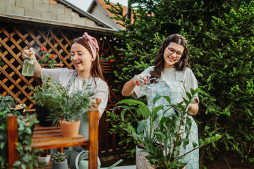 Two female friends or sisters taking care of plants with water can and mister	
