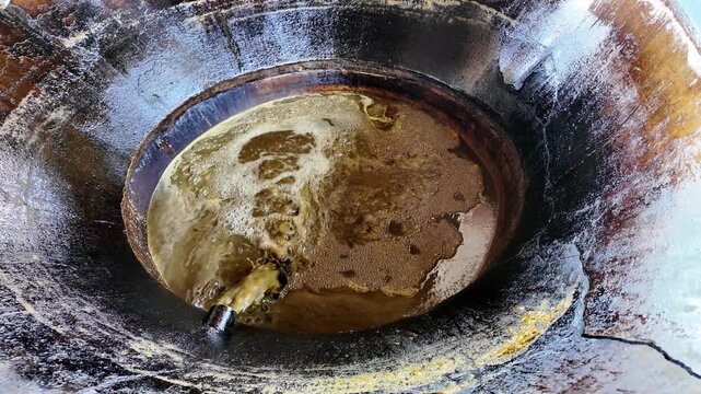 Boiling sugarcane juice for jaggery in rustic metal vat, bubbling with heat and motion