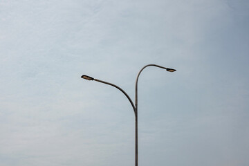 Minimalist view of a modern forked street light against a pale, cloudy sky. This image symbolizes...