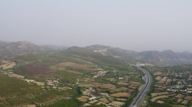 Aerial shot of Kallar Kahar valley, highway winding through patchwork fields and hills. Punjab, Pakistan