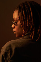 Black young adult woman wearing glasses turning head to side, showing profile and dreadlocks,...
