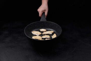 Hand holding a frying pan with sizzling chicken fillets, showcasing cooking process against a dark...