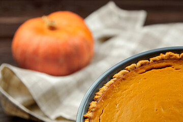 Freshly baked pumpkin pie in a blue ceramic dish, with a vibrant orange pumpkin in the background, showcasing autumn flavors and seasonal culinary delights