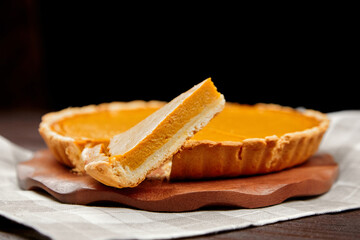 Pumpkin pie on wooden serving board with slice removed, showcasing creamy filling and flaky crust, perfect for autumn gatherings and festive celebrations
