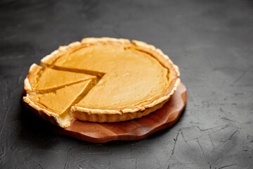 Pumpkin pie on a wooden serving board with a slice removed, showcasing the creamy filling and flaky crust, perfect for autumn celebrations and festive gatherings