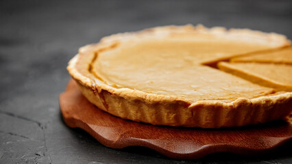 Delicious pumpkin pie on a wooden serving board, showcasing a perfectly baked crust and smooth filling, invitingly sliced to reveal its rich texture and flavor profile