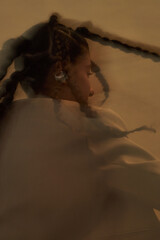 Black woman with braided hair sitting with back turned, head slightly tilted, wearing earrings,...