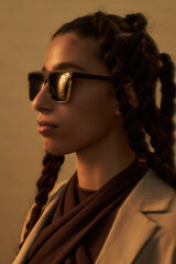 Young adult Middle Eastern woman wearing sunglasses standing in profile with braided hair, looking...