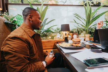 Focused people collaborate during a casual lunch. The setting features greenery and laptops,...