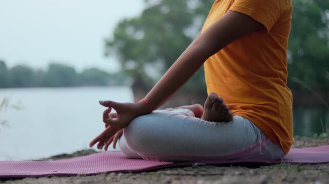 Close up shot of a woman sitting in padmasana pose near a lake during blue hour twilight.