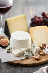 Board of different cheeses with nuts, figs, grapes and wine on wooden table