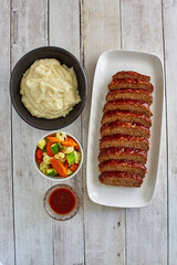 glazed meatloaf and mashed potatoes served with steamed vegetables, overhead without brush
