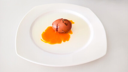 Cracked brown egg with yolk on white plate