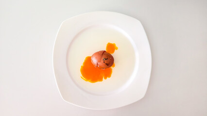 Cracked brown egg with yolk on white plate