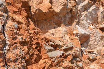 A vibrant, close-up view of a rugged rock face showcases an array of warm earthy tones, ranging from deep reddish-browns to lighter oranges and beiges, with pronounced cracks and shadows