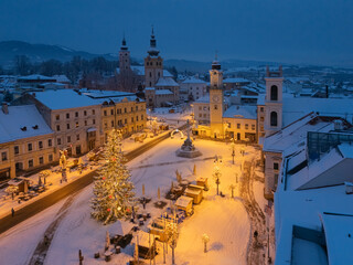 Aerial view of a snow-covered square, adorned with a Christmas tree and illuminated by warm lights, contrasting against the dusk, BanskÃ¡ Bystrica, BanskobystrickÃ½ kraj, Slovakia.