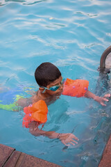 Happy Indian boy swimming in a pool, Kid wearing swimming costume along with air tube during hot summer vacations, Children boy in big swimming pool.