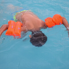 Happy Indian boy swimming in a pool, Kid wearing swimming costume along with air tube during hot summer vacations, Children boy in big swimming pool.