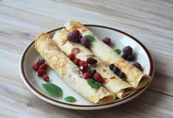 Plate of fresh pancakes. Pancakes decorated with wild strawberries, purple raspberries, blueberries and herb leaves.