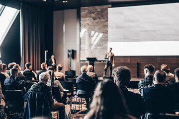 Speaker giving a talk in conference hall at business event. Rear view of unrecognizable people in...