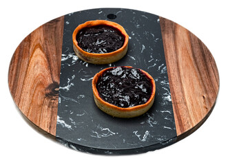 Mini berry jam tarts with rustic shortcrust pastry shells on a black marble and wooden serving...