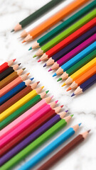 Colorful pencils arranged in two groups on a white marble surface in a close up studio shot