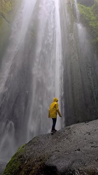 Discover the breathtaking Gljufrabui canyon Iceland waterfall as a traveler walks along the rocky path, wearing a vibrant yellow rain jacket. Mist fills the air, creating an enchanting atmosphere.